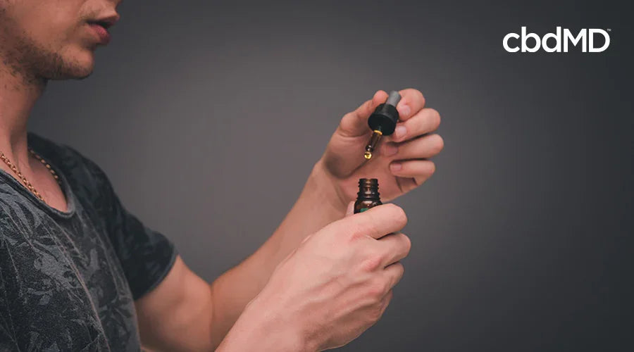 Man using a dropper bottle to take CBD oil drops against a neutral background