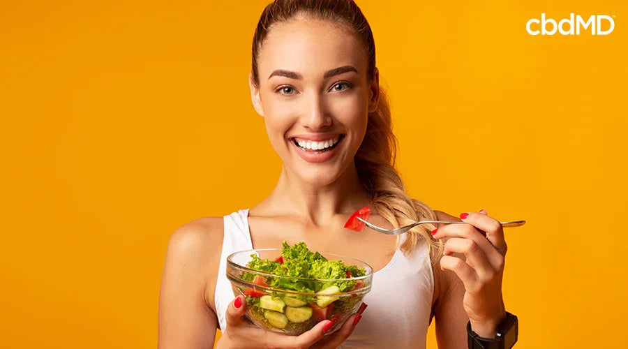 Smiling woman eating fresh salad with greens and tomatoes against vibrant yellow background