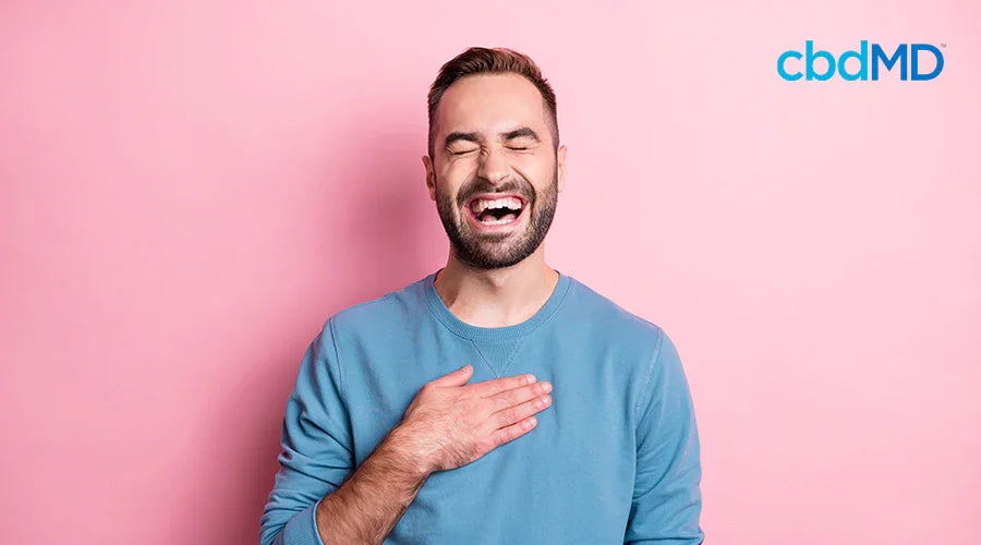 Smiling man in blue sweater laughing with hand on chest against pink background