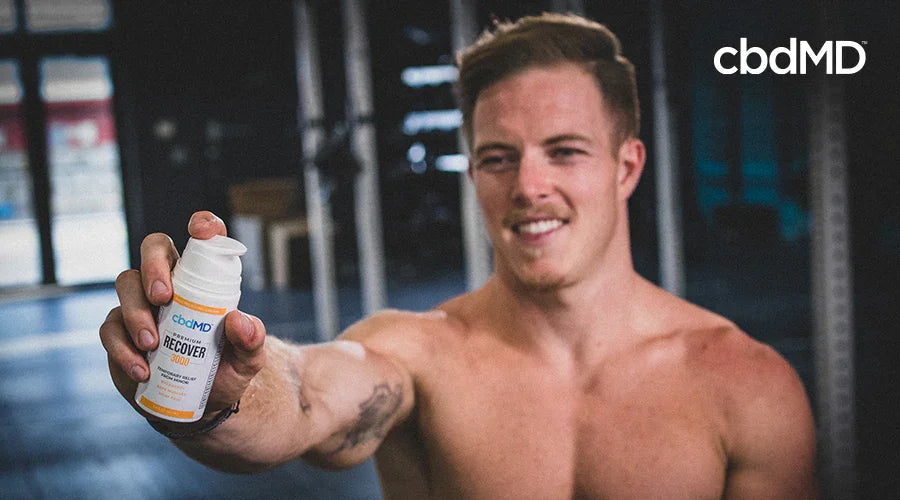 Athlete holding cbdMD Recover cream in gym, sports recovery wellness product