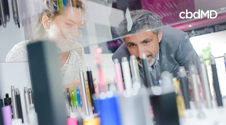 Two people looking at assorted vape pens and cartridges in a glass display case