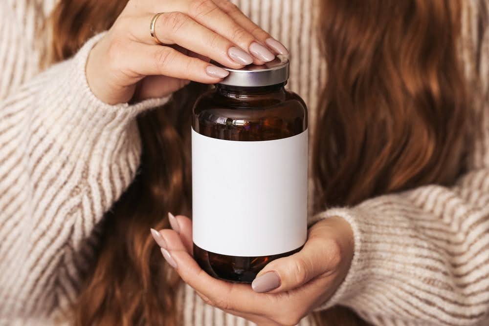 close-up of woman holding a brown supplement bottle with a blank, white label