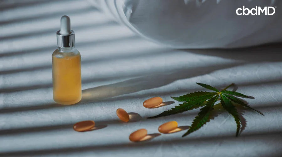 CBD oil dropper bottle, capsules, and cannabis leaf on a bed for sleep support