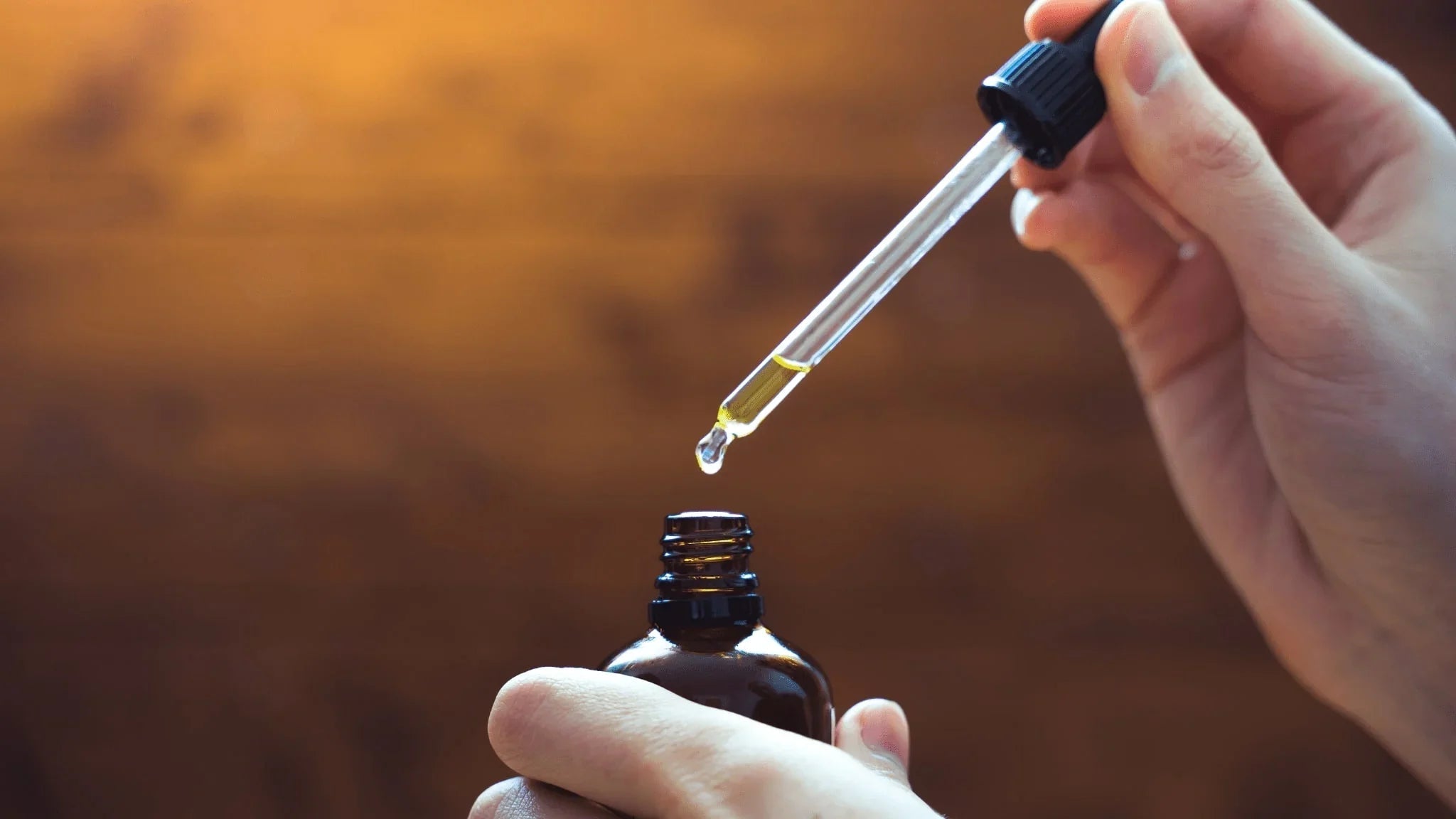 close-up of a hand holding a dropper with cbd oil over a tincture bottle