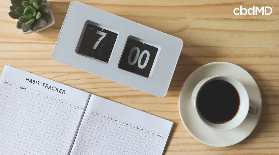 Habit tracker notebook, clock showing 7:00, coffee cup, and succulent on wooden desk