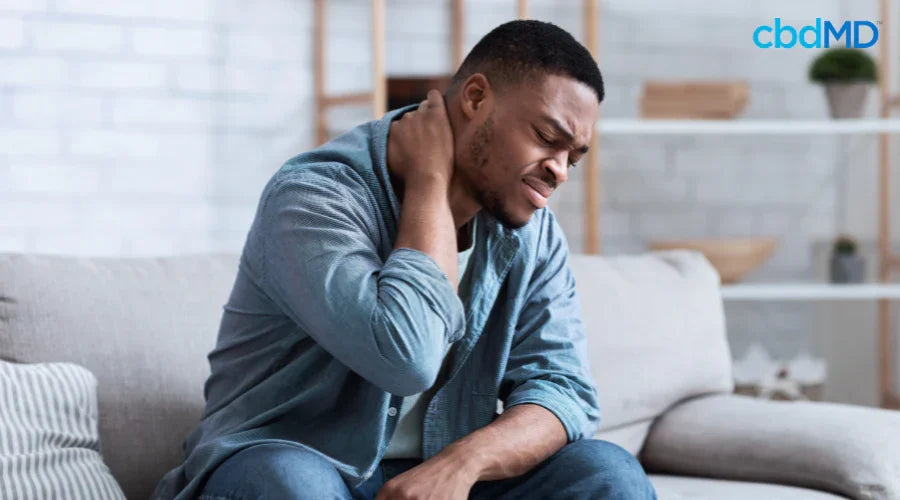 Man sitting on couch holding neck, showing discomfort, seeking natural pain relief.