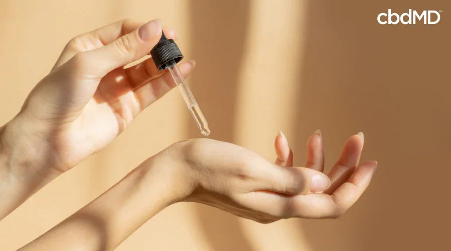Person applying CBD oil to skin with dropper for skincare wellness