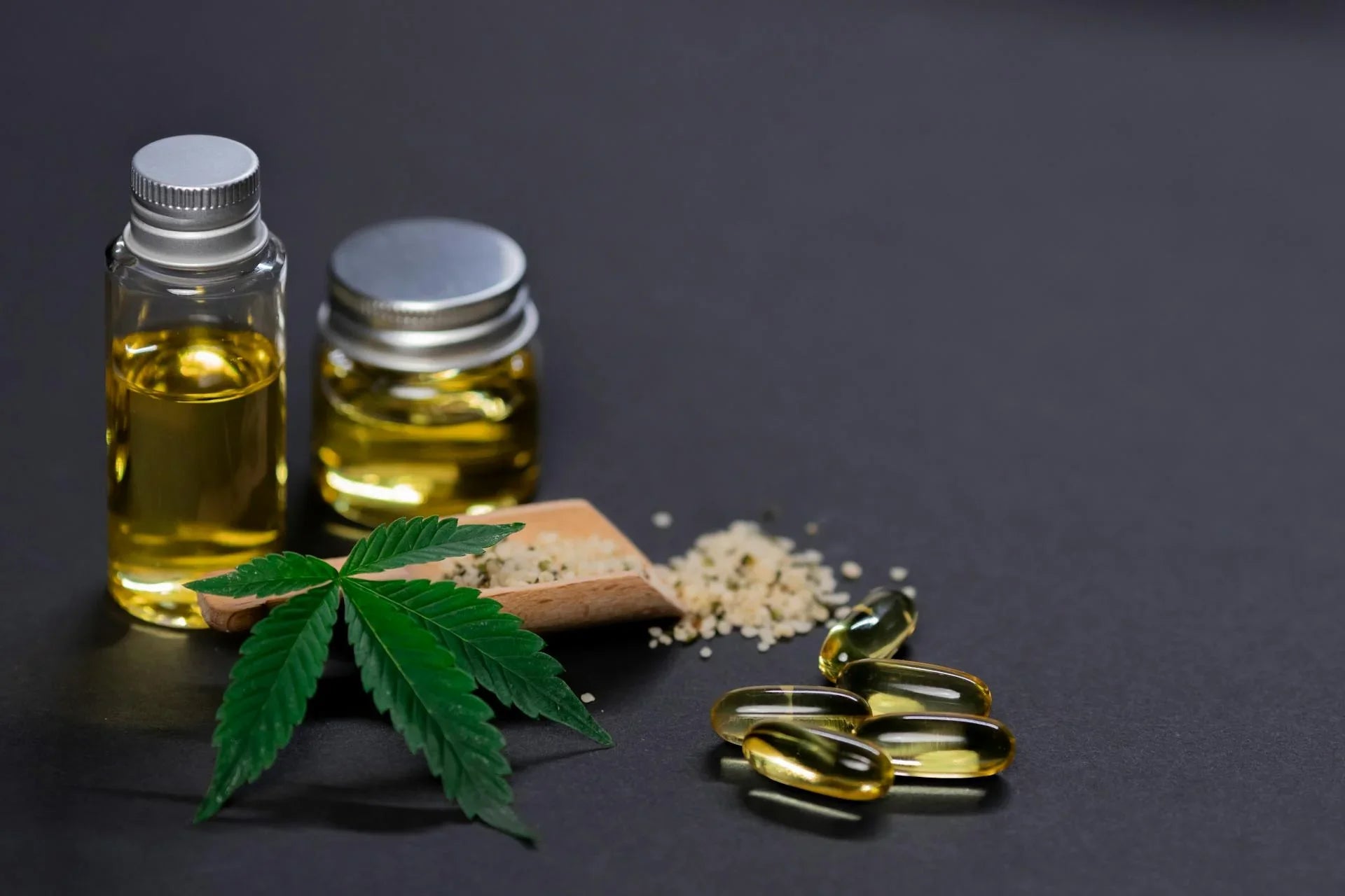 Hemp leaf, oil bottles, capsules, and seeds on black background for CBD wellness