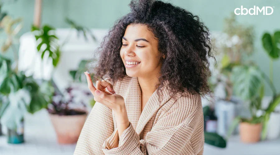 Smiling woman in robe applying wellness product, surrounded by indoor plants, relaxing at home