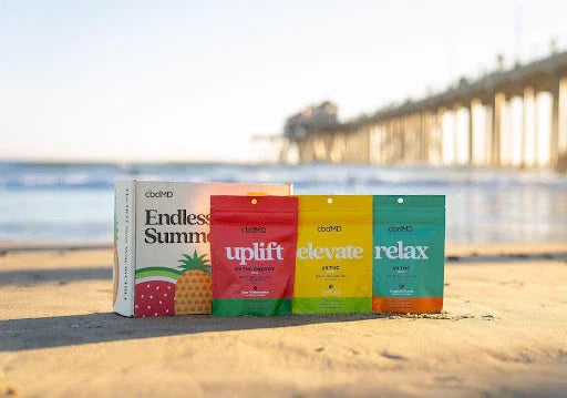 cbdMD wellness gummies and supplement packs on sandy beach near ocean and pier