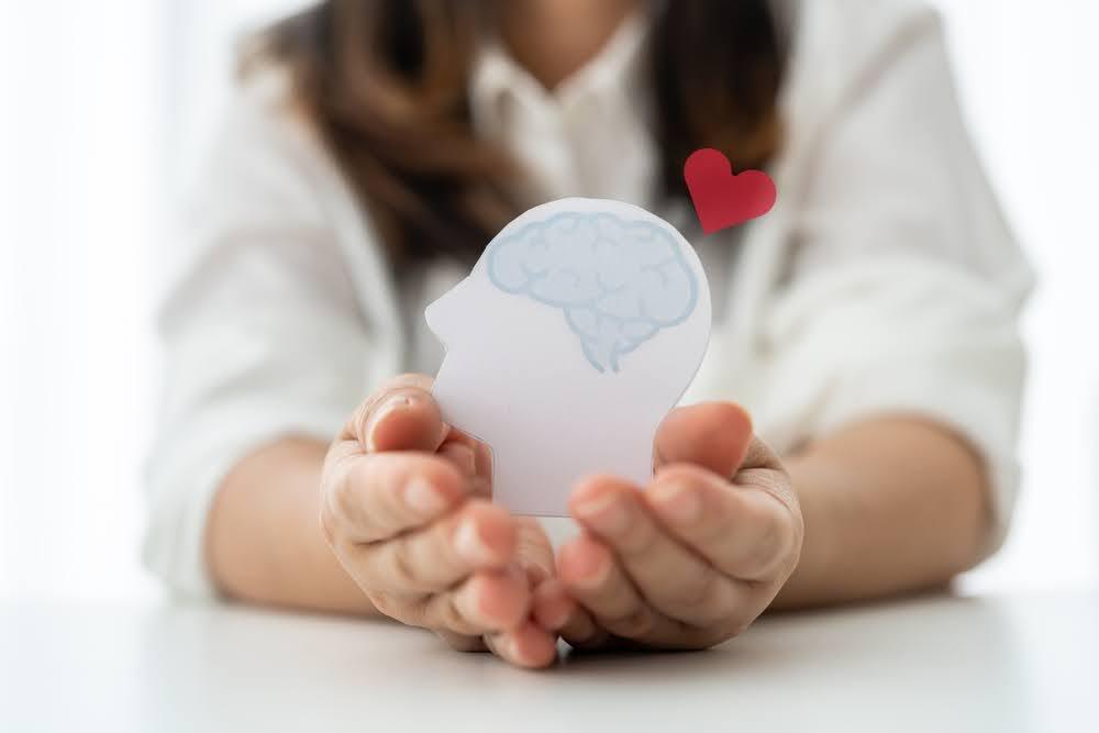closeup of a woman holding a cutout of a head and brain with a heart hovering above
