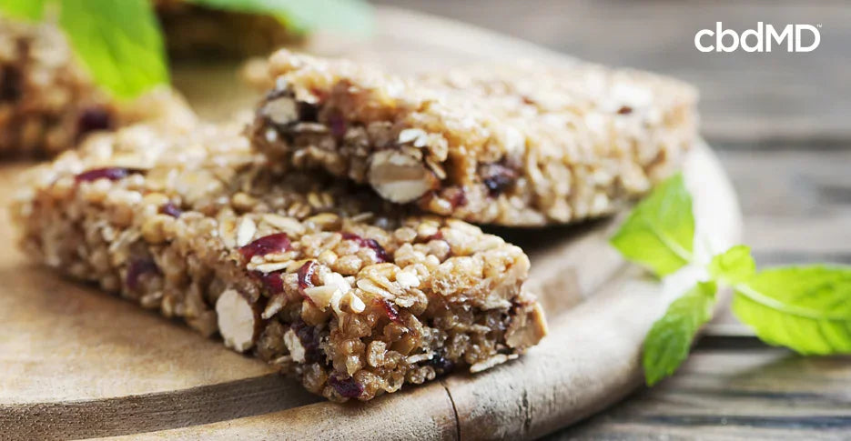 Close-up of protein bars with nuts and seeds on a wooden board, fresh mint leaves nearby.
