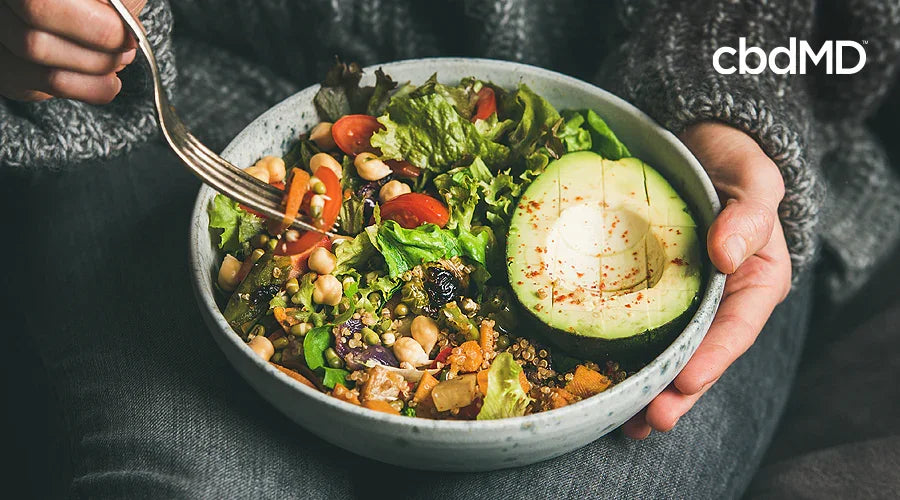 Fresh salad bowl with avocado, cherry tomatoes, leafy greens, and beans held in hands