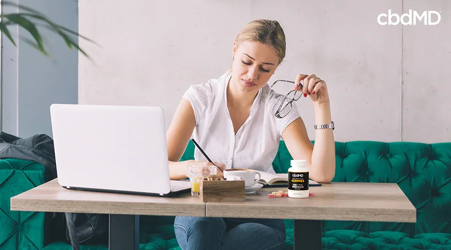 Woman working at desk with laptop and CBD gummies, promoting stress relief and wellness.
