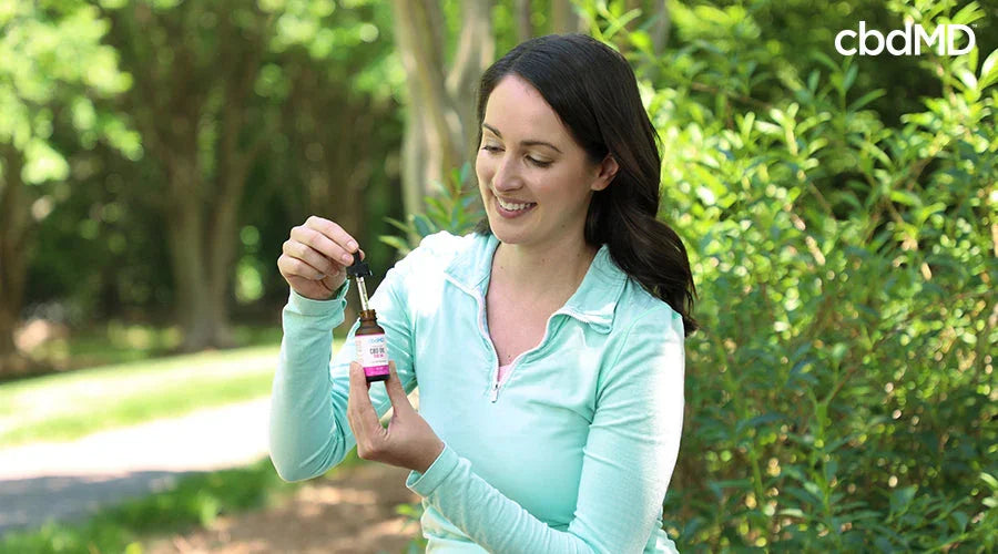 A woman outside taking a dropper out of premium cbd oil berry - cbdMD