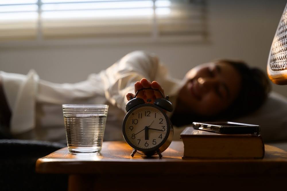 woman turning off her alarm clock on her nightstand