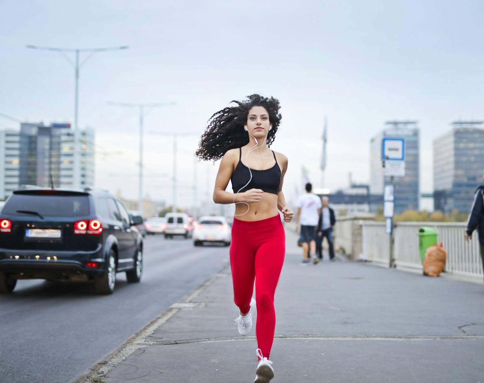 woman running towards the camera with earbuds in on the sidewalk