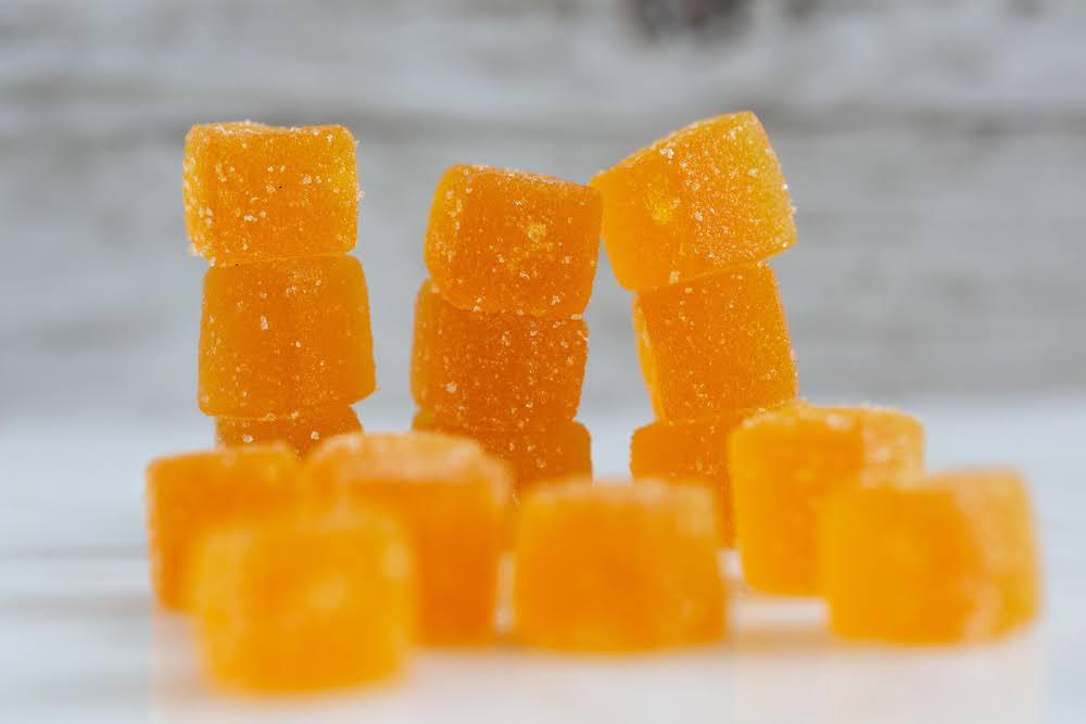 closeup image of orange-colored cbd gummies on a white countertop