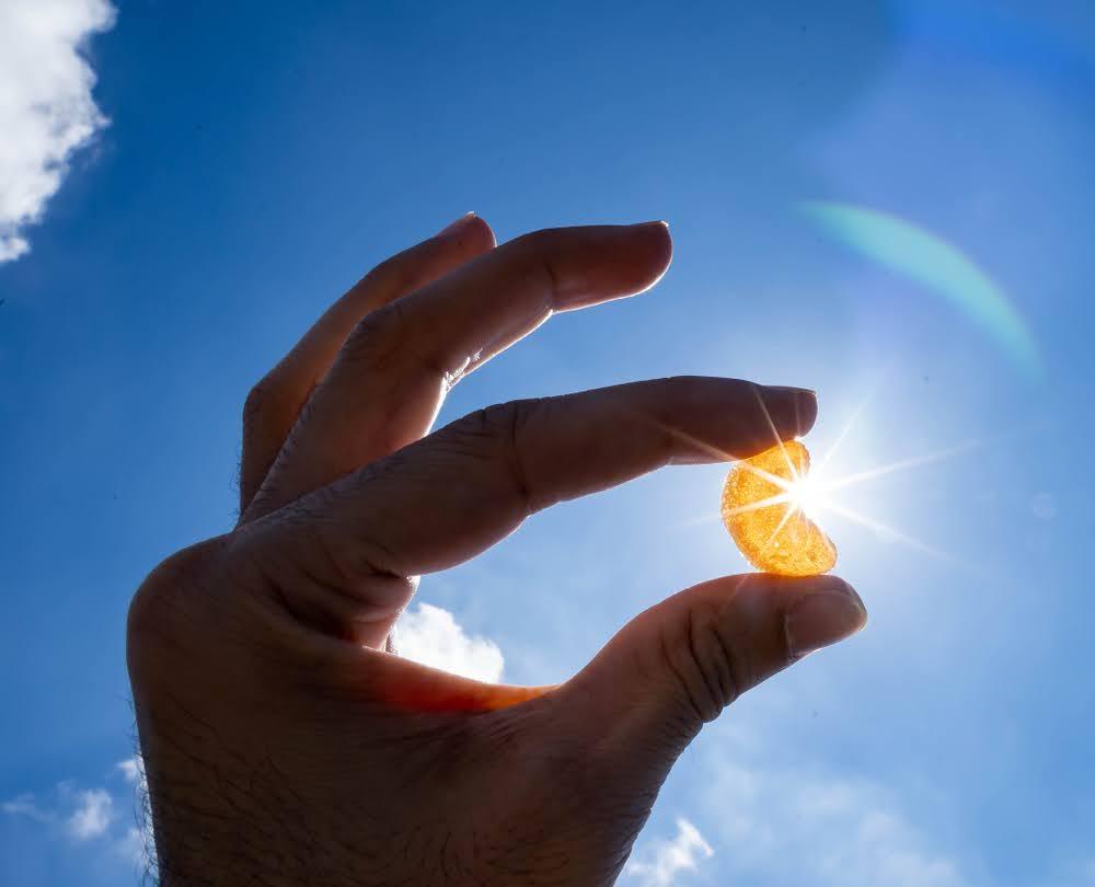 Hand holding a CBD gummy against the bright blue sky in sunlight