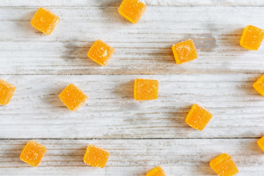 Yellow CBD nano gummies cubes scattered on a white wooden surface