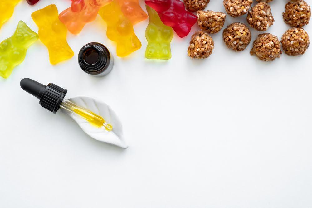 Assorted colorful gummies, dropper bottle, and snack bites on white background