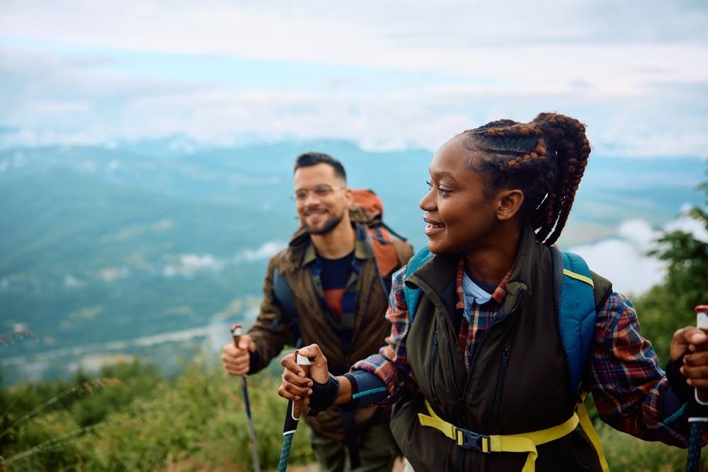 woman and man on a hillside hiking with walking sticks and backpacks