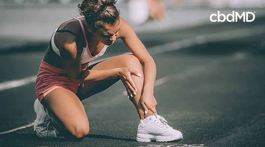 Female athlete in sportswear holding her ankle on a track, showing discomfort or pain.