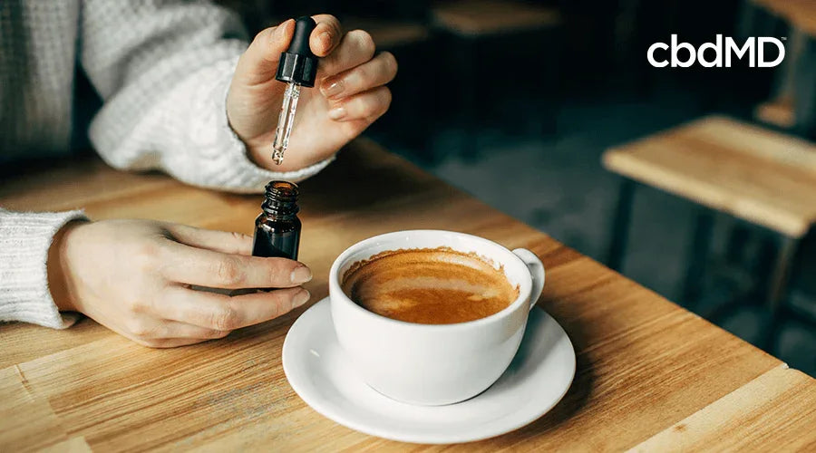 Person adding tincture drops to a cup of coffee at a café table