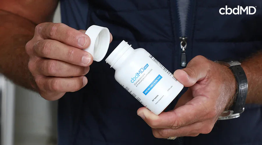 A man holding max for pain 200 mg cbd 4 mg thc tablets in his hand while taking the lid off - cbdMD