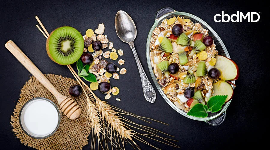 Healthy breakfast bowl with oats, kiwi, apple, grapes, milk and honey on black background