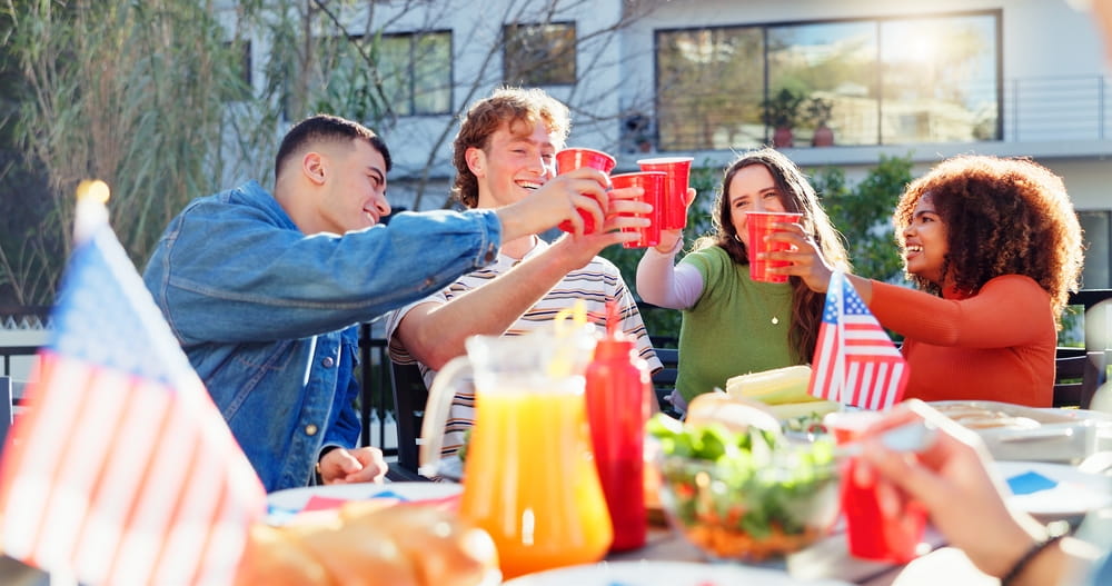 group of friends toasting cups at an outdoor feast for the Fourth of July 