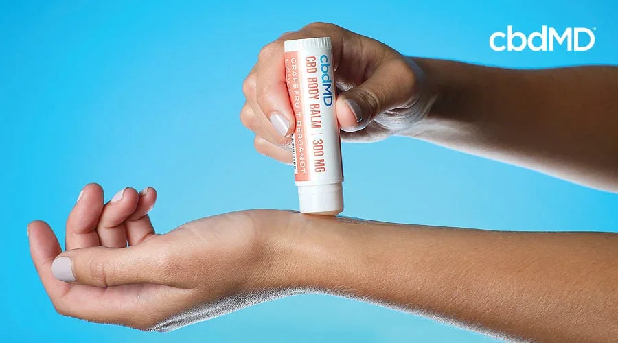 Applying CBD body balm stick to wrist, grapefruit bergamot, on blue background