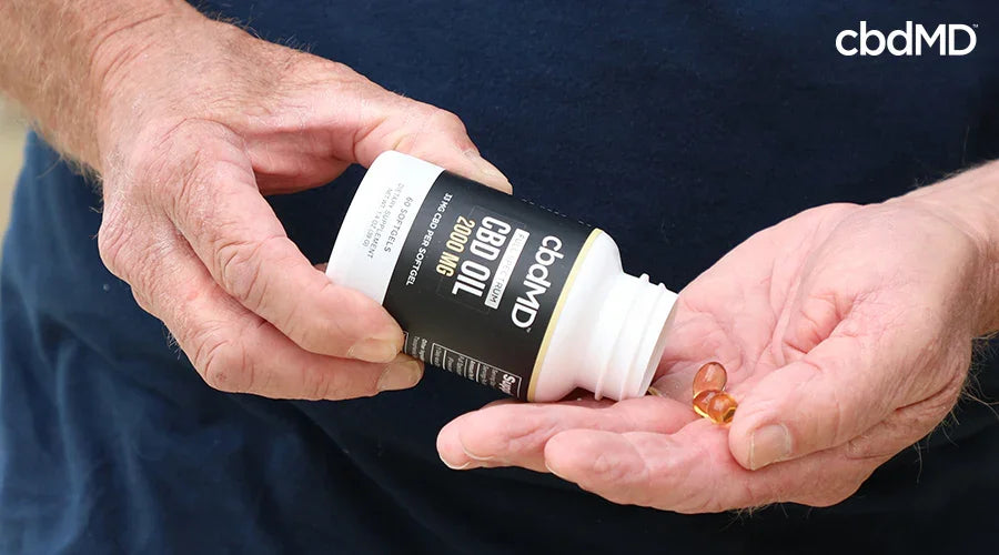 Hands holding CBD oil softgel capsules and a labeled CBD oil bottle