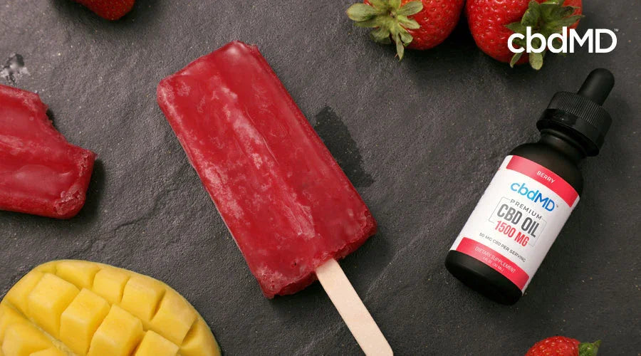 cbdMD oil tincture bottle on a counter alongside red fruit popsicle and sliced mango