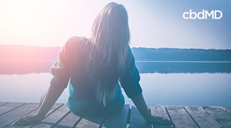Woman relaxing by a peaceful lake on a wooden dock, enjoying calm wellness lifestyle
