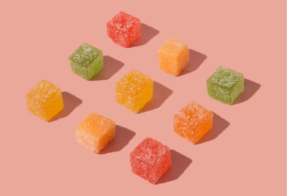 Assorted fruit-flavored gummies with sugar coating on a pink background