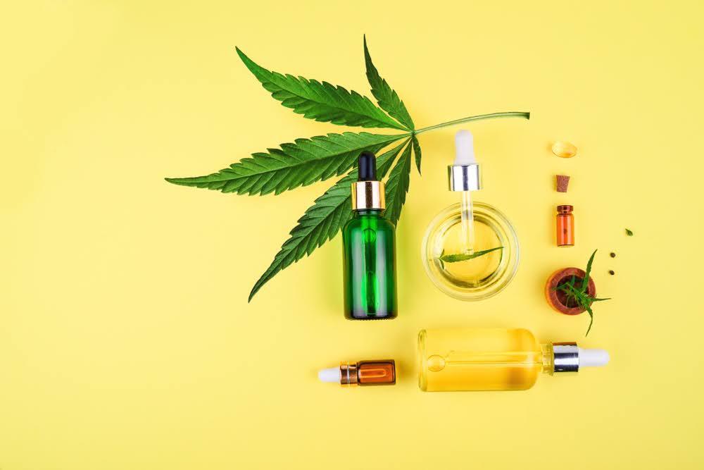 Assorted hemp wellness products with oil droppers and leaf on yellow background