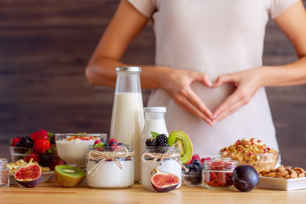woman making heart sign with her hands over her stomach with a table of fruits and granola in front of her