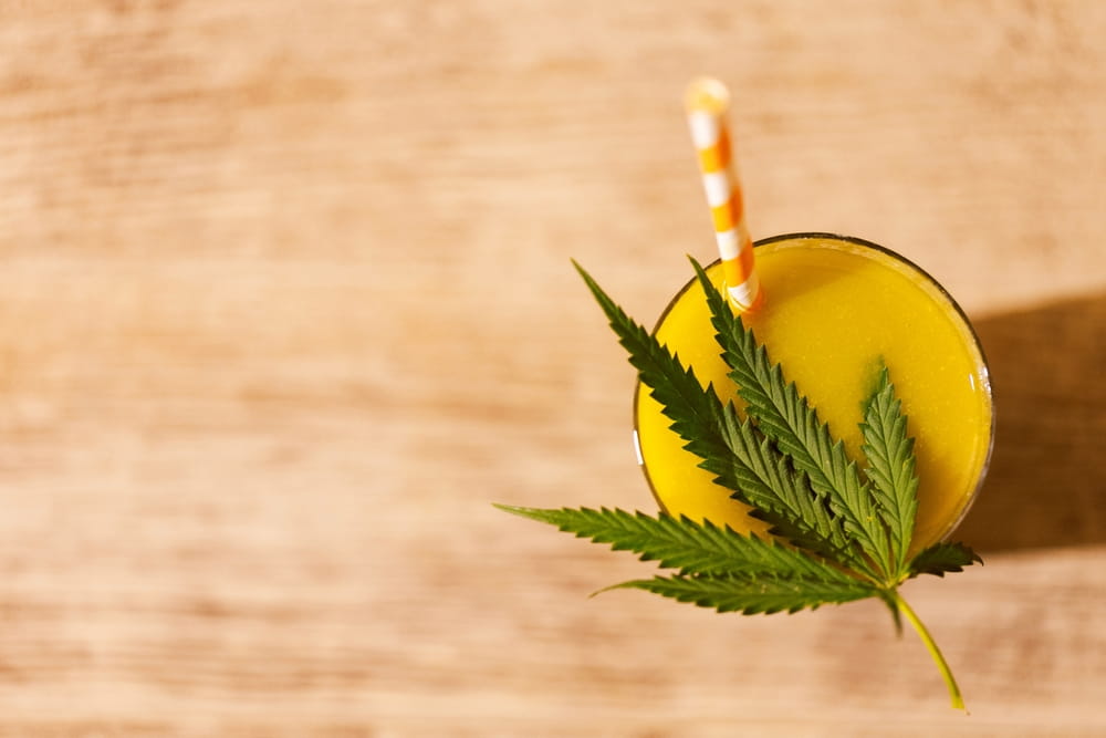 orange drink with a straw topped off with a hemp leaf