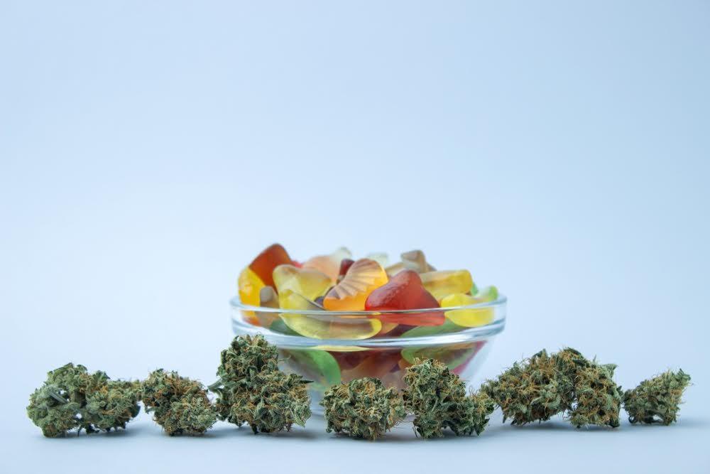 Bowl of colorful gummies with hemp flower buds on white background