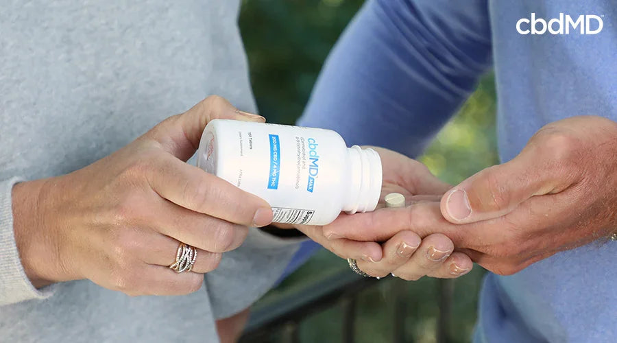 Person pouring CBD capsules from a white bottle into another hand outdoors