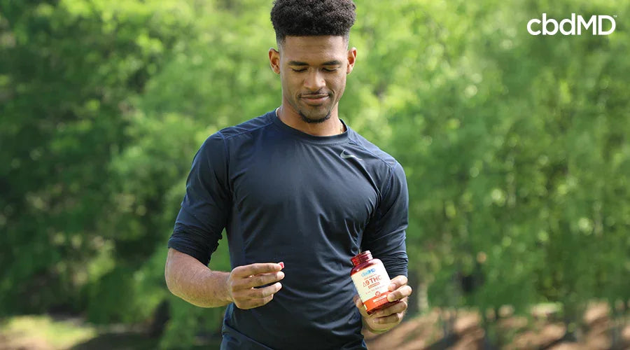 man in a field holding a cbdMD bottle in one hand and a delta 9 gummy in the other