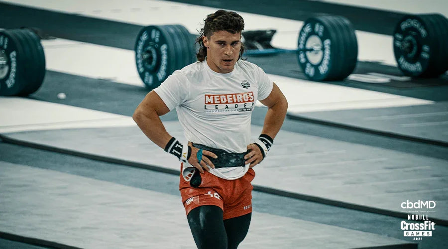 Male athlete in CrossFit event, wearing a lifting belt, weights in background, indoor gym