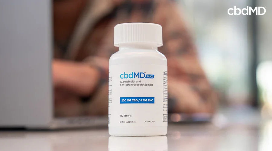 Max for pain 200 mg cbd 4 mg thc tablets with a person working on a computer in the background - cbdMD
