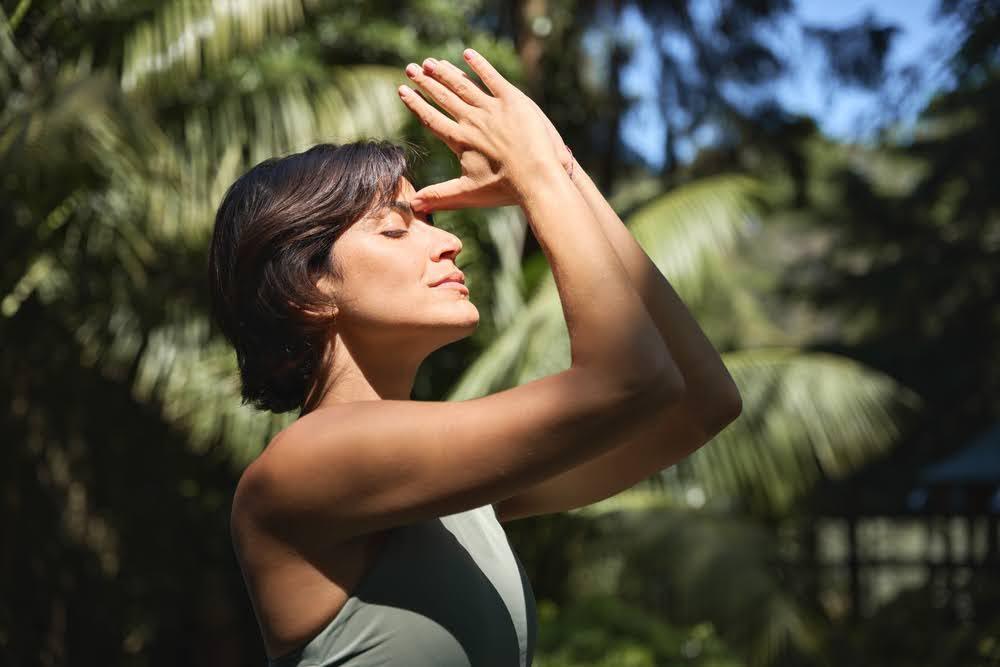 Woman practicing deep breathing exercise outdoors in nature with sunlight and palm trees