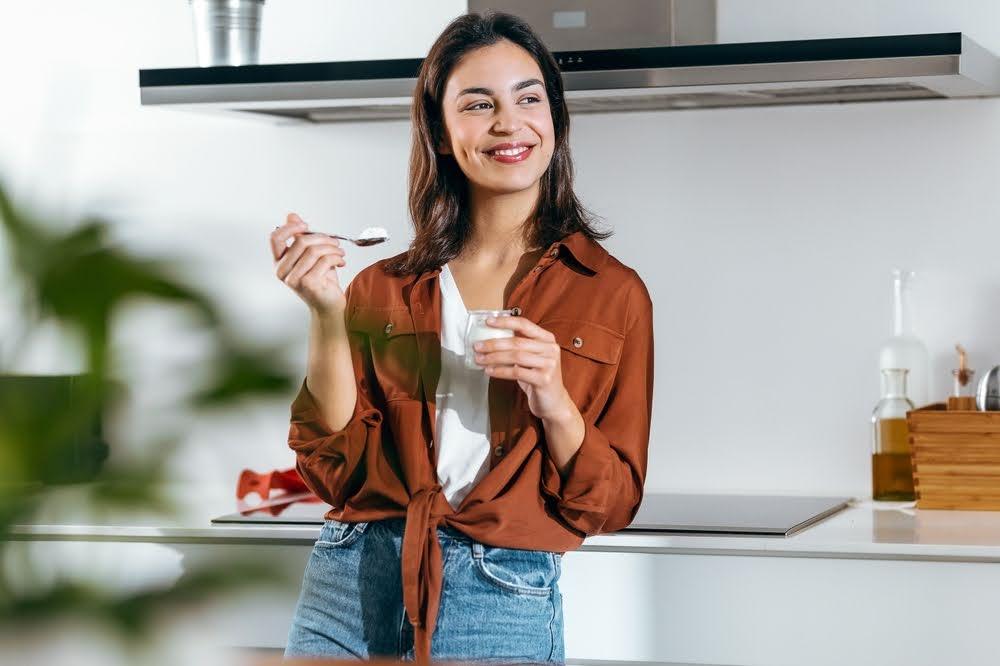 woman standing against a counter in a kitchen eating yogurt