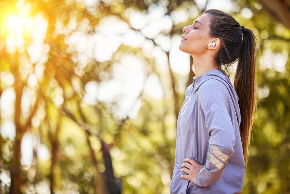 woman in running gear standing in front of trees taking a deep breath